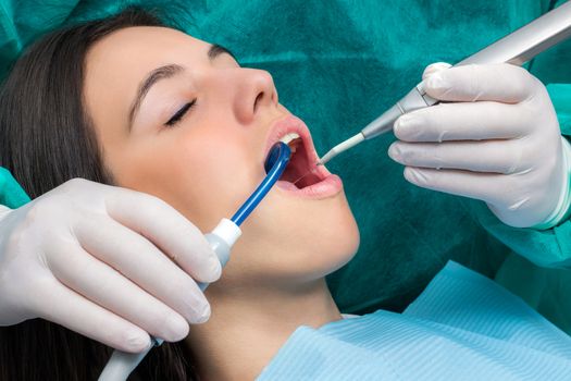 Close up macro face shot of young woman having dental cleaning.Hands wearing gloves working on teeth with saliva ejector and water cleaning unit.