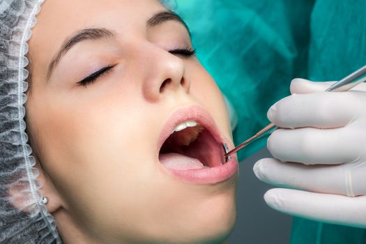 Close up macro face shot of woman being prepared for dental surgery.Hand with glove doing check up with mouth mirror on teeth.