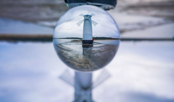 White Windmill at end of coast full of puddles near Baltic sea in Swinoujscie in reflection of crystal ball