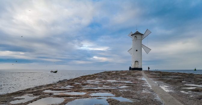 White Windmill at end of coast full of puddles near Baltic sea in Swinoujscie
