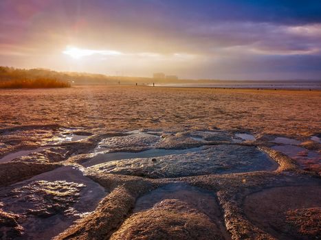 Beautiful sunset over beach in Swinoujscie near Baltic sea with stones and puddles at bottom