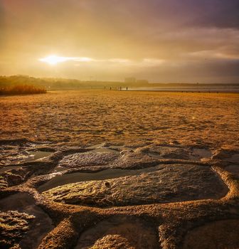 Beautiful sunset over beach in Swinoujscie near Baltic sea with stones and puddles at bottom