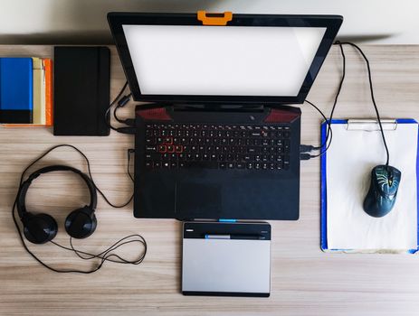 Flat lay of desk with laptop, notebook, powerbank, headphones and graphic tablet