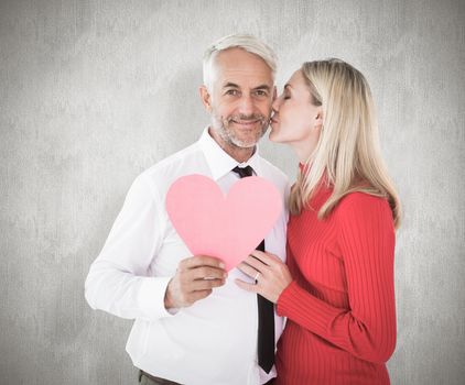Handsome man holding paper heart getting a kiss from wife against weathered surface 