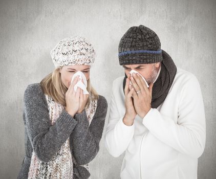 Sick couple in winter fashion sneezing against weathered surface 