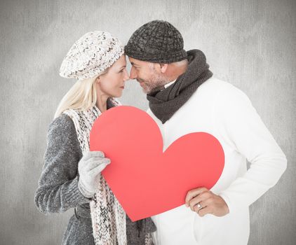 Smiling couple in winter fashion posing with heart shape against weathered surface 
