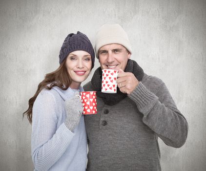 Happy couple in warm clothing holding mugs against white background