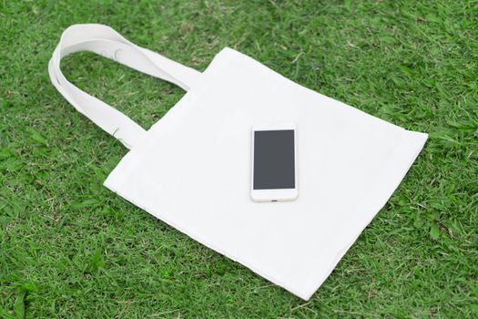 Closeup white bag canvas fabric with smartphone on green grass background, Save the world concept