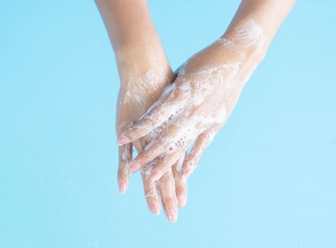 Closeup woman's hand washing with soap on blue background, health care concept