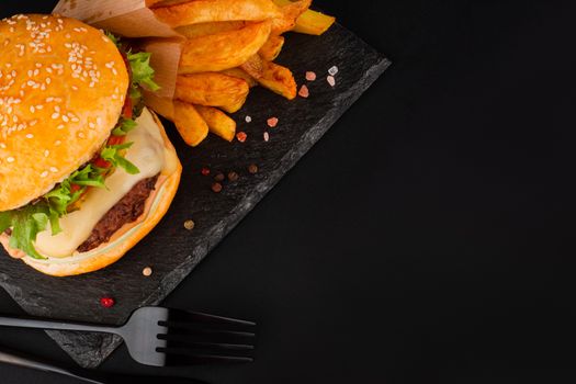 One big tall classic hamburger burger cheeseburger with french fries on black stone plate on black background with copy space for text