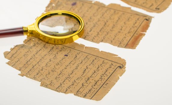 Book pages with an Arabic manuscript on a table with a light and a magnifying glass. Paleography, the study of ancient Arabic writing