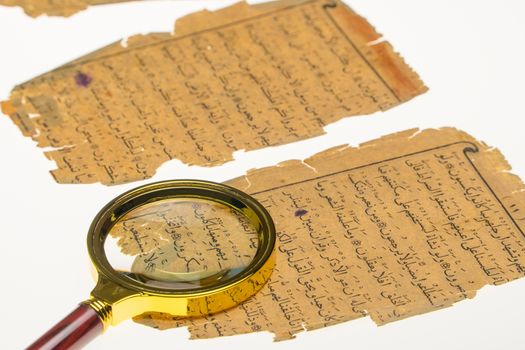 Book pages with an Arabic manuscript on a table with a light and a magnifying glass. Paleography, the study of ancient Arabic writing