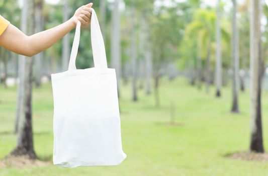Closeup woman hand holding white bag canvas fabric with green nature background, Save the world concept