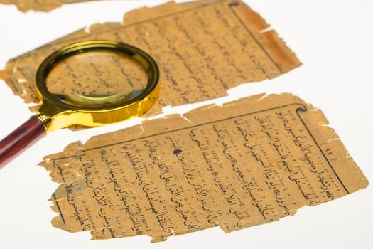 Book pages with an Arabic manuscript on a table with a light and a magnifying glass. Paleography, the study of ancient Arabic writing
