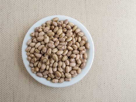 White plate with handful of raw carioca beans on a light cloth towel.