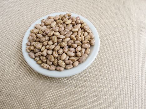 White plate with handful of raw carioca beans on a light cloth towel.