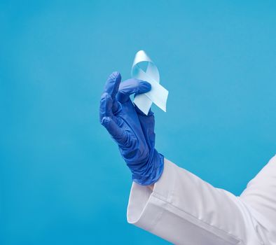 female hand holds blue silk ribbon in the shape of a loop on a blue background, symbol of the fight and treatment of prostate cancer