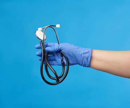 doctor in a white medical coat holds a black stethoscope on a blue background, close up