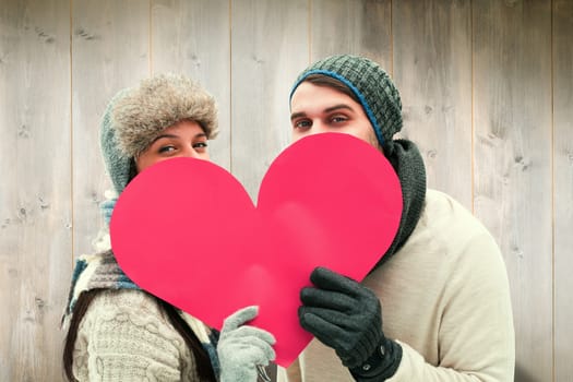 Attractive young couple in warm clothes holding red heart against wooden planks