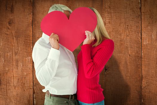 Couple embracing and holding heart over faces against wooden planks