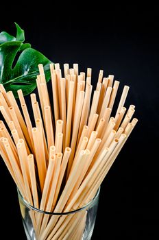 Wheat straw for drinking water in glass with green leaf on black background. Zero waste concept.