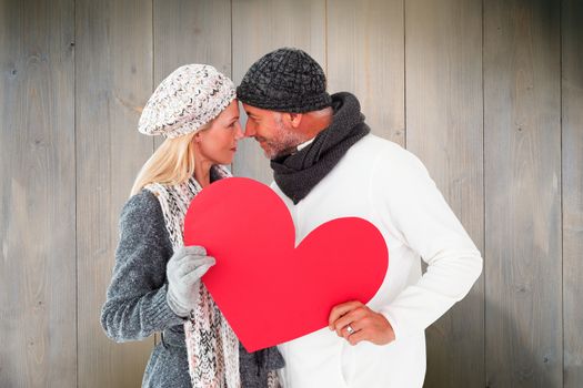 Smiling couple in winter fashion posing with heart shape against wooden planks