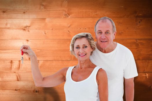 Mature couple smiling at camera with new house key against overhead of wooden planks