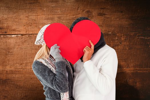 Couple in winter fashion posing with heart shape against overhead of wooden planks