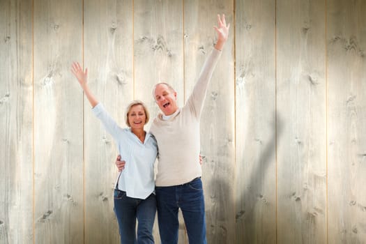 Happy mature couple cheering at camera against pale wooden planks