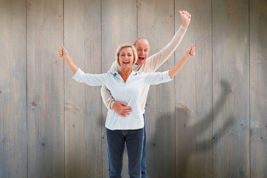 Happy mature couple cheering at camera against pale grey wooden planks