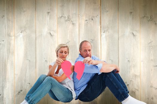 Sad mature couple holding a broken heart against pale wooden planks