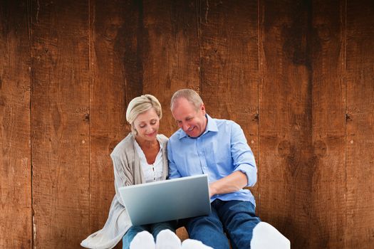Happy mature couple using laptop against weathered oak floor boards background