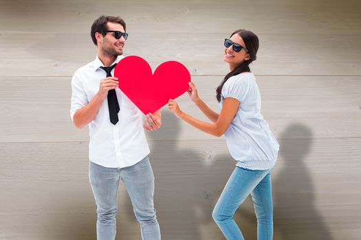 Hipster couple smiling at camera holding a heart against bleached wooden planks background