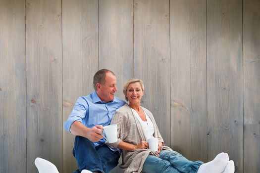 Happy mature couple having coffee against pale grey wooden planks