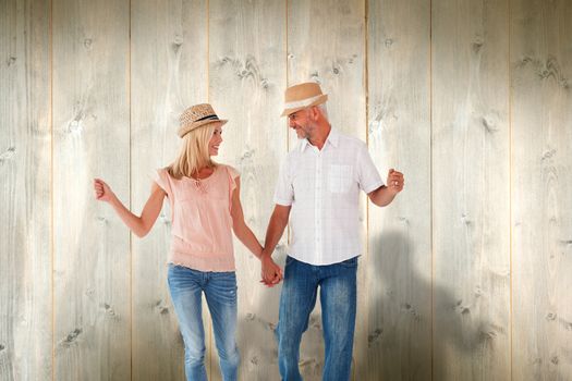 Happy couple walking holding hands against pale wooden planks