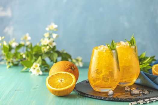 Two glass of orange ice drink with fresh mint on wooden turquoise table surface. Fresh cocktail drinks with ice fruit and herb decoration. Alcoholic non-alcoholic drink-beverage.