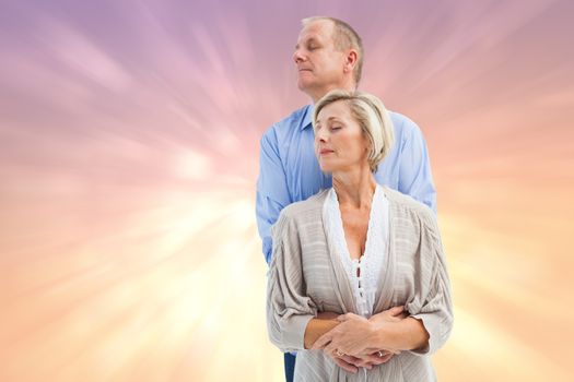 Happy mature couple embracing with eyes closed against pink abstract light spot design