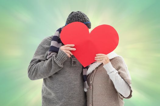 Happy mature couple in winter clothes holding red heart against green abstract light spot design