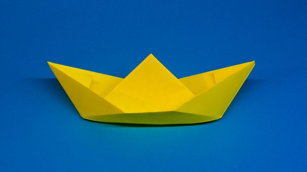 Origami, yellow ship of paper on blue background, hobby