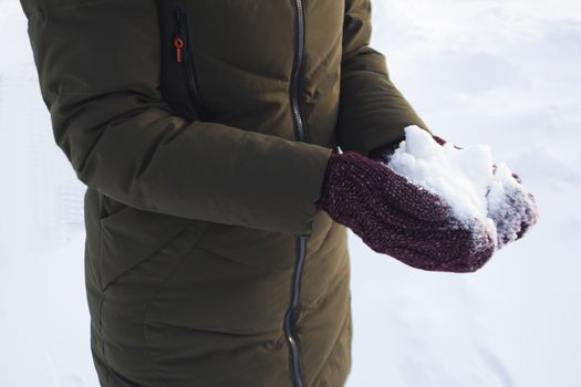 Young girl holding snow in her hands in mittens, winter, fun, joy, sports, recreation, children