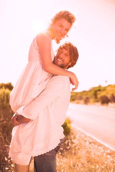 Attractive man lifting up his girlfriend smiling at camera on a sunny day