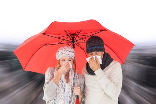 Couple in winter fashion sneezing under umbrella against high angle view of city
