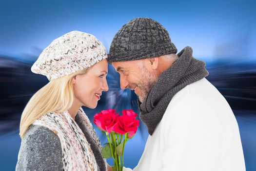 Smiling couple in winter fashion posing with roses against mirror image of city skyline