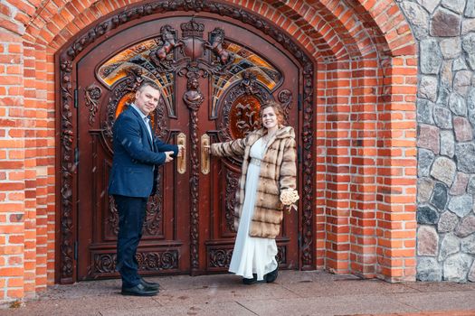 newlywed couple standing near door of castle in the city park on early spring snowy day