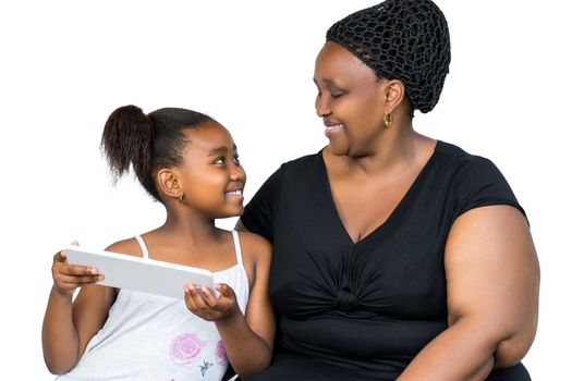 Close up portrait of little african girl and mother having fun together with digital tablet isolated on white background.Mother and daughter looking at each other.