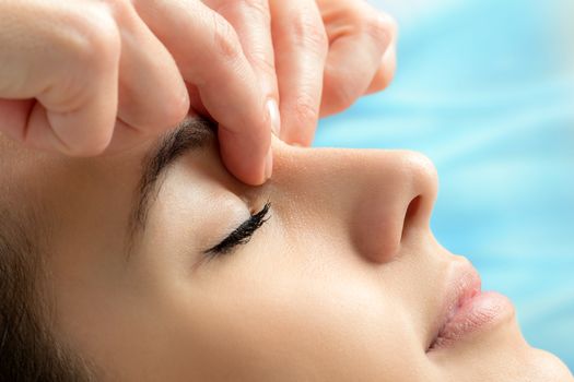 Extreme close up of hands applying pressure between eyes on young woman.Therapist relieving emotional tension touching sensitive areas on face.