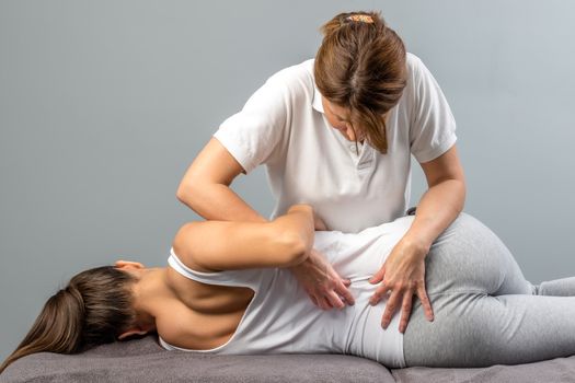 Female physiotherapist doing manipulative spine treatment on young patient.