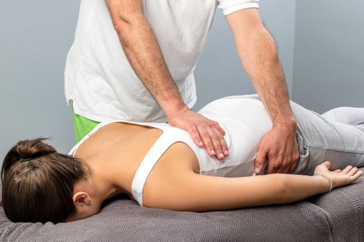 Close up of male osteopath doing manipulative massage on female lower back.