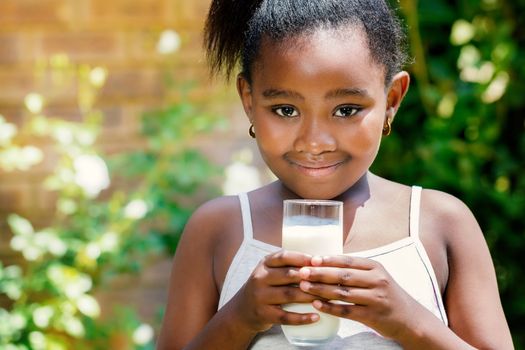 Close up portrait of cute little african girl holding glass with milk in garden.