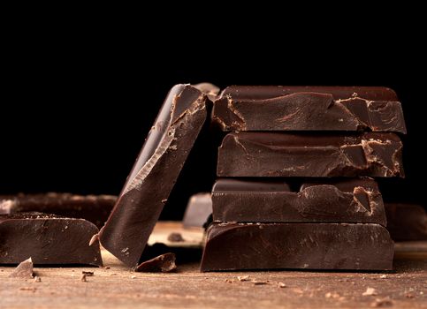 broken black chocolate on a wooden table, culinary sweet ingredient, close up